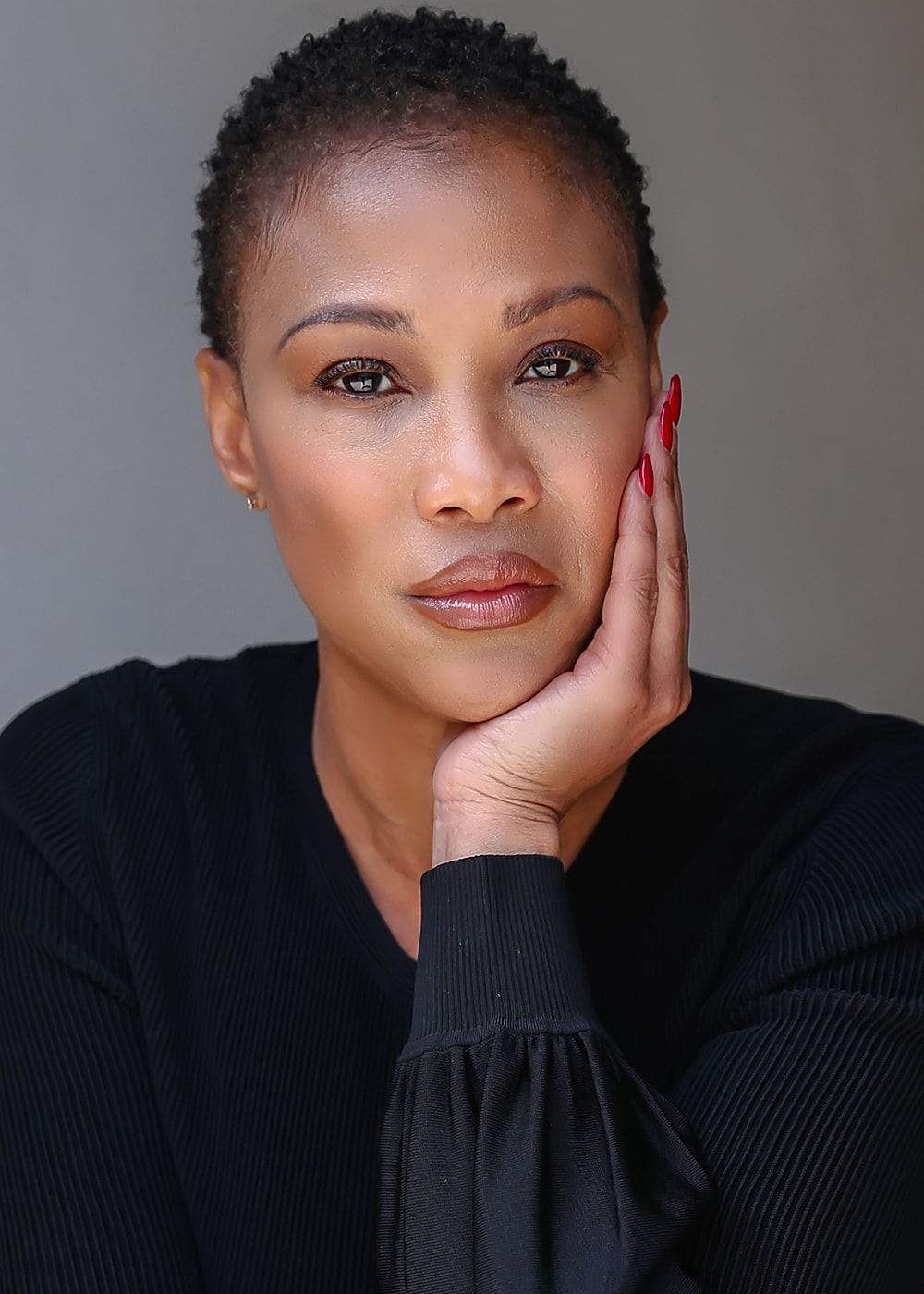 Woman with short hair resting her chin on hand.